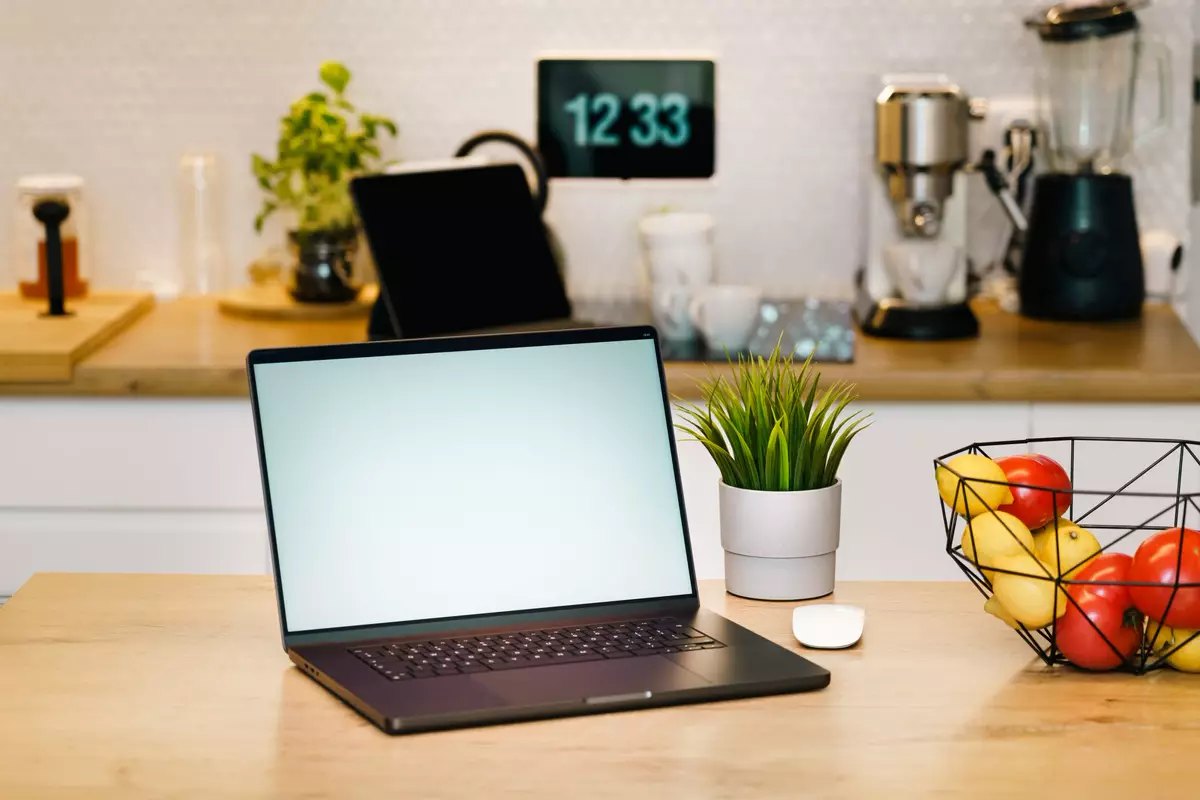 Geöffneter Laptop auf einem Tisch vor einer eingerichteten Küche für die digitale Küchenplanung